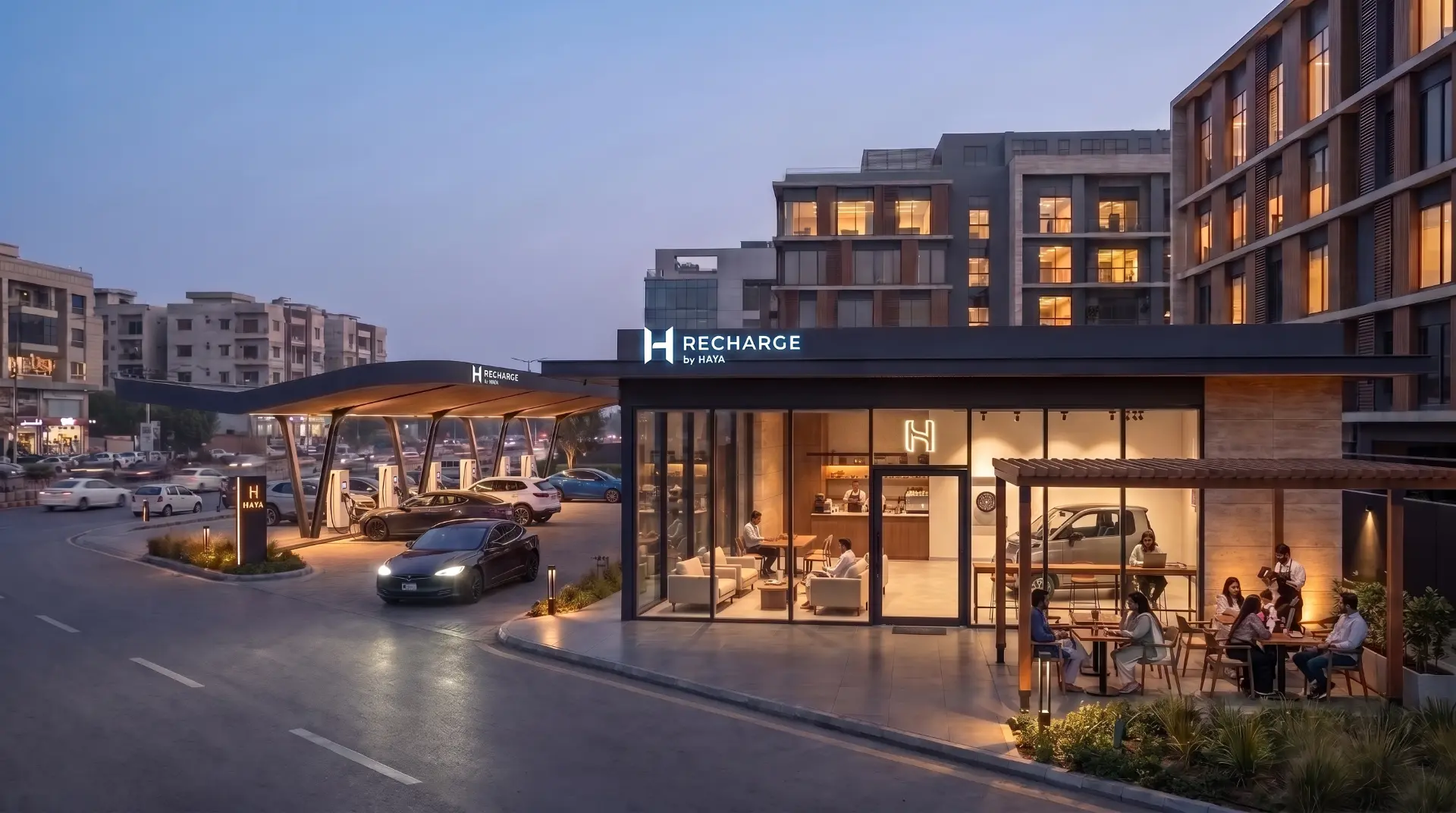 A RECHARGE by HAYA station at dusk, with guests relaxing in the lit café pavilion and an EV pulling away from the charging canopy